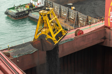 Loading coal from cargo barges onto a bulk vessel using ship cranes  in offshore coal cargo terminal.
