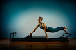 © Georgii - Young girl doing pilates exercises with a reformer bed. Beautiful slim fitness trainer on reformer gray background, low key, art light. Fitness concept