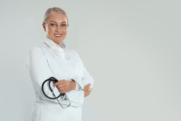 Wall Mural - Portrait of mature doctor with stethoscope on light grey background. Space for text