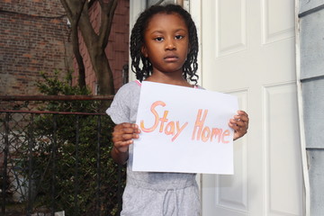 Kid holding Stay Home sign outdoors near white house door