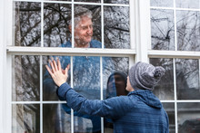 Teen Visiting Senior Citzen Quarantined In Home, Touching Hands Through The Window
