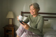 morning lifestyle portrait of attractive and happy middle aged woman on her 50s having coffee on bed using internet mobile phone relaxed and cheerful enjoying social media app