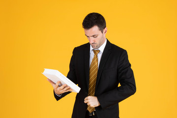 Portrait of a handsome businessman wearing white suit and tie while holding a book with yellow background.