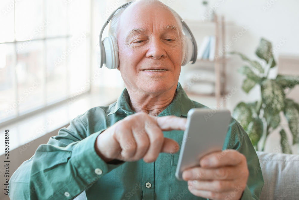 Elderly man with mobile phone and headphones at home