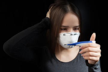 Poster - Elevated temperature is a symptom of coronavirus. Young woman in antibacterial medical mask looks at a thermometer on a black background