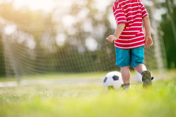 Little boy playting football on the field with gates