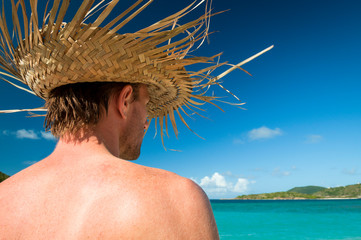 Wall Mural - Tourist wearing woven palm frond hat standing in front of a vibrant blue tropical island paradise