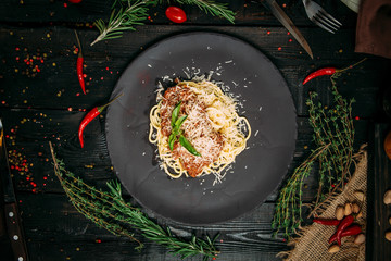Wall Mural - Top view on bolognese pasta with parmesan on a black plate on the dark wooden background, horizontal