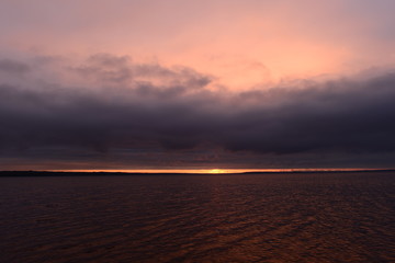 Wall Mural - Thunderstorm cloud in sunlight on sunset in the bright ominous sky on the horizon over water