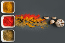 Three White Square Jars Of Various Spices On A Gray Chopping Board. Next To Them Are Scattered Spices And Garlic