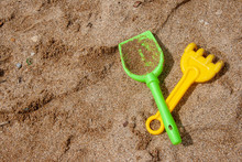 Bright Plastic Children's Toys In The Sand. Concept Of Beach Recreation For Children. Children's Summer Games. Summer Concept. Flat Lay, Top View, Copy Space. Shovel And Rake In The Sand.