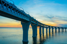 The Highway Over The Water. The Road Against The Sunset. Road Bridge Over The Water On The Background Of Sunset. The Expressway Passes Over The Bridge. The Bridge In The Background Of The Morning Sky.