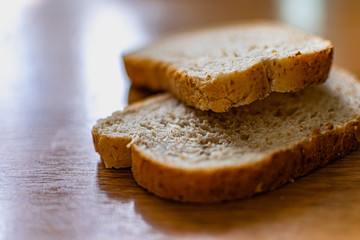 Two sliced slices of bran bread with a crisp crust of rye flour, lying on a brown wooden table, after fresh baking in the kitchen in the sunlight