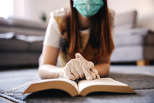 Woman In Home Isolation Wearing Face Mask And Gloves, Reading A Book And Studying Information About Coronavirus Outbrake 2020. Home Education During Quarantine.