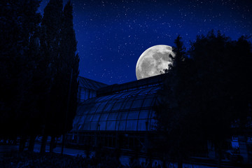 Mountain night landscape of building at forest at night with moon or vintage country house at night with clouds and stars. Cold autumn night