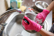 Woman in rubber gloves washing up dishes and pot
