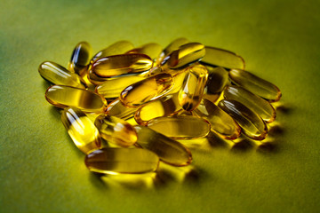 Fish oil capsules are scattered on the yellow surface.