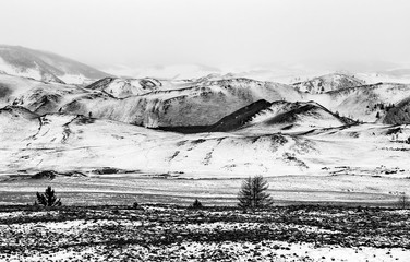 Rocky hills covered with snow in cloudy weather in black and white in Siberia