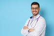 Close-up portrait of smiling handsome young male doctor with stethoscope around neck, wearing white coat and eyeglasses, isolated on blue background