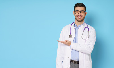 Horizontal banner of smiling young male doctor showing and presenting something with hand, isolated on blue background with copy space on left