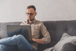 © vladdeep - Caucasian young man freelancer working from home. Sitting with laptop on sofa. Surfing internet sites or working.