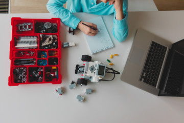 kid building robot from plastic blocks and programming it with computer