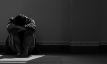 Sunlight And Shadow On Surface Of Hopeless Man Sitting Alone With Hugging His Knees On The Floor In Empty Dark Room In Black And White Style