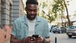 © Sofiia - Young african american attractive man using phone walk on street smile sunlight sunset cellphone computer fashion internet face outside technology businessmen black city mobile summer