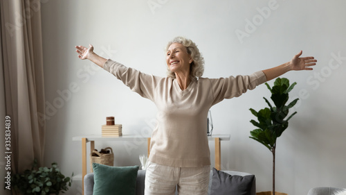 Fotografía Excited elderly mature retired woman dancing in living room with widely opened outstretched arms, enjoying freedom