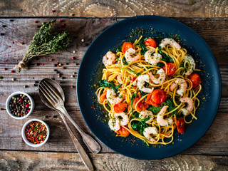 Spaghetti with prawns and vegetables on wooden background