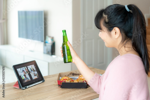 Asian woman virtual happy hour meeting party and drinking alcohol beer online together with her friend in video conference with digital tablet for a online meeting in video call for social distancing