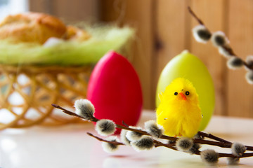  Happy easter background, copy space. Yellow chick sitting on a willow branch. Baking, red and green Easter egg in the background. Eggs and chicken as Easter symbol. Easter greet. Homemade bakery. 