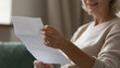 Close up wrinkled female hands holding paper document. Smiling happy middle aged senior woman reading letter, feeling excited by good news, final banking loan credit mortgage payment notification.