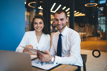 Portrait of cheerful corporate employees sitting at table with modern technology and smiling at camera, confident professional analysts enjoying briefing meeting for cooperation on business project