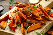 Healthy Baked Orange Sweet Potato wedges with dip sauce, herbs, salt and pepper on wooden board