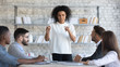 © fizkes - Serious african american businesswoman manager speaks in boardroom at meeting. Diverse female mentor presentation new project for colleagues in conversation. Woman employee communicating with team.