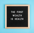 © IRINA - The first wealth is health. Motivational quote on black letter board on blue background. Concept Health Care and Medicine, inspirational quote of the day