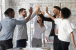 © fizkes - Excited successful multiracial business people giving high five, celebrating win. Good teamwork result concept. Happy employees team engaged in team building activity at corporate meeting.