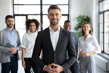 Portrait headshot of happy businessman in suit looking at camera. Different smiling ethnicity businesspeople standing behind of male company chief business owner. Leader of multi-ethnic team concept.