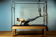 © Georgii - Young girl doing pilates exercises with a reformer bed. Beautiful slim fitness trainer on reformer gray background, low key, art light. Fitness concept