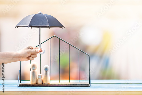 Woman hand hold open the black umbrella for protect to family wood put in the house model on sunlight in the public park, Loan or saving money for property protection  real estate and a lover concept.