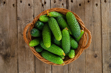 Wicker basket with cucumbers on an old wooden table.