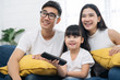© saksit - Happy Asian family spending time by watching tv together on sofa in living room. family and home concept
