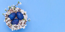Blue Easter Eggs In A Basket With Flowers On A Blue Background. Horizontal Photograph. Top View