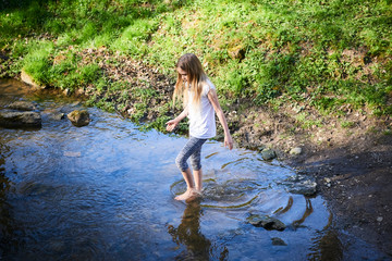 Wall Mural - Child cute blond girl playing in the creek. Girl walking barefoot in forest stream  and exploring nature. Summer children fun. Children summer activities
