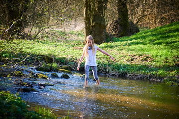 Wall Mural - Child cute blond girl playing in the creek. Girl walking barefoot in forest stream  and exploring nature. Summer children fun. Children summer activities
