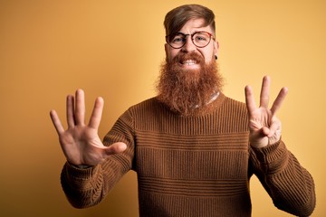 Handsome Irish redhead man with beard wearing glasses and winter sweater over yellow background showing and pointing up with fingers number eight while smiling confident and happy.