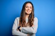 © Krakenimages.com - Young beautiful brunette woman wearing casual sweater standing over blue background happy face smiling with crossed arms looking at the camera. Positive person.