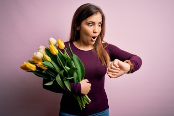 Poster - Young blonde woman holding romantic bouquet of yellow tulips flowers over pink background Looking at the watch time worried, afraid of getting late