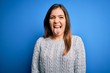© Krakenimages.com - Beautiful young woman wearing casual wool sweater standing over blue isolated background sticking tongue out happy with funny expression. Emotion concept.